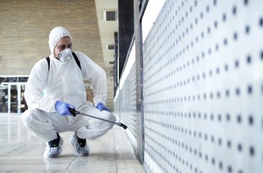 Shot of male person in white chemical protection suit doing disinfection of public areas to stop spreading highly contagious corona virus. Stop coronavirus or COVID-19.